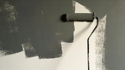 An image of a paint roller, partially painting a white wall with dark gray paint.