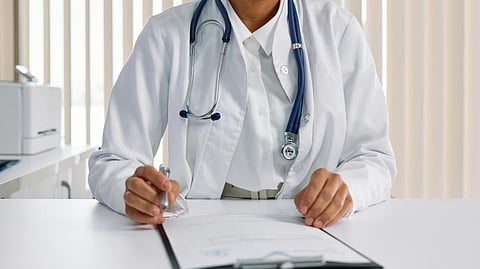 An image of a doctor and writing pad on table.
