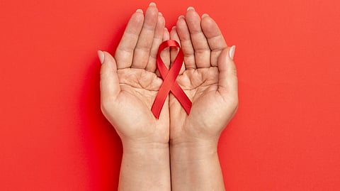 An image of hands gently cupping a red awareness ribbon on a solid red background.