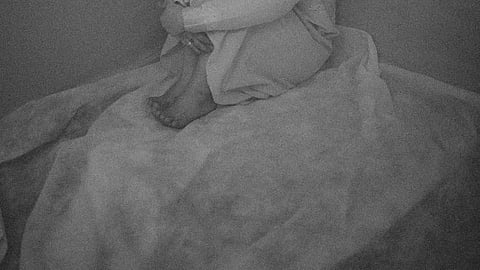 Black and white image of a woman sitting on bed in very sad mood.