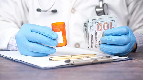 An image of a doctpr holding medicine in one hand and money in other.