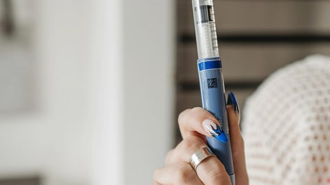 Image of a woman with long nails holding an injection pen.