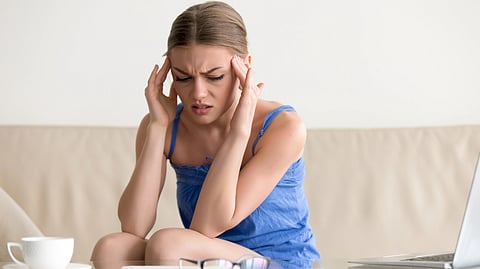 An image of a woman sits on a couch, resting her head in her hands.