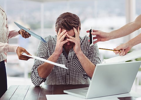 A man at a desk stressed because so many hands pointing at him with files, pencils etc. 