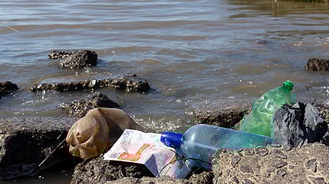 Shoreline with plastic bottles, bags, and litter scattered on rocks.