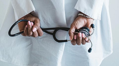 An image of a person in a white coat, holding a stethoscope behind their back. 