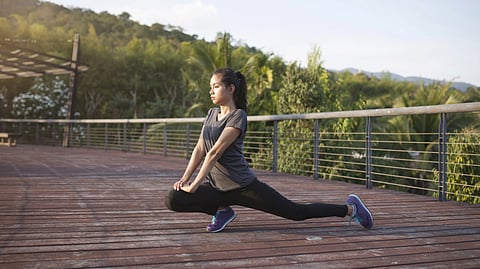 A Chinese looking woman doing lunges outside on a road. 