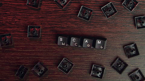 The word “scam” spelled out using wooden letter blocks placed on a table.