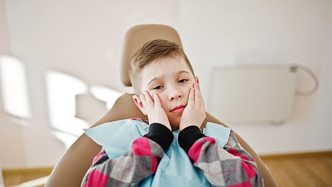 A child in the dental chair holding his face in hands indicating dental pain. 