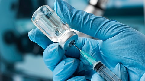 Close-up of gloved hands inserting a syringe into a vial.