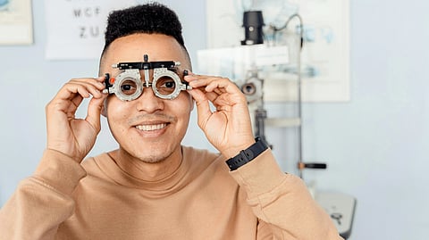 A smiling person wearing a pink sweatshirt holds an eye testing device.