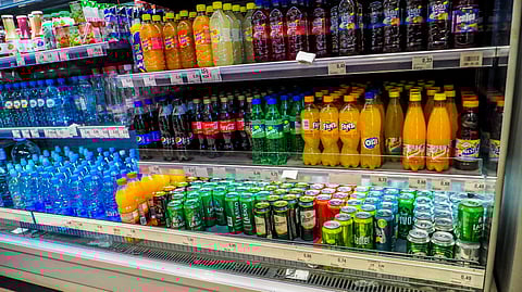 Supermarket fridge displaying various bottled and canned drinks, including soda, water, and juice.