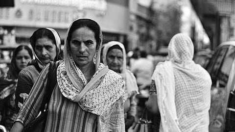 Black and white portrait of women in traditional attire walking on a busy street.