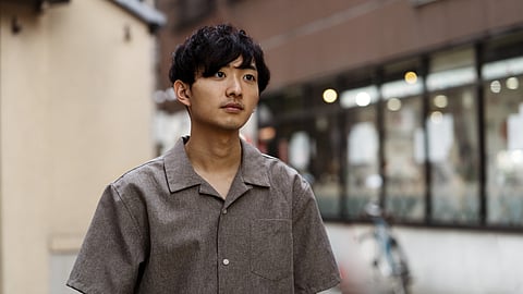 Young man with short dark hair wearing a gray shirt.