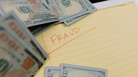 A yellowish paper with the word “FRAUD” stamped on it, placed beside stacks of U.S. dollar bills.
