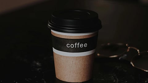A brown plastic takeaway coffee cup labelled with coffee placed on a table.