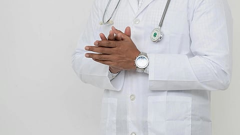 Close-up of a doctor’s hand wearing a silver watch with a stethoscope resting on a white apron.