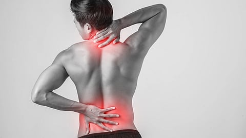 A man holding his lower back and back neck due to pain. Those areas are highlighted red.