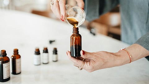 A person pours liquid into a small brown bottle on a white countertop.