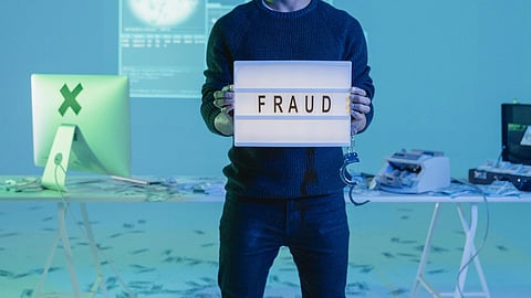 Close-up illustration of a man holding a poster reading “Fraud” while wearing black shirt and jeans.