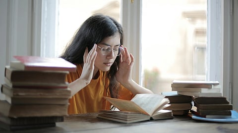 Young woman in glasses and yellow shirt sitting at a table with stacks of books.
