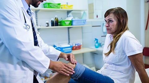A doctor examines a patient's knee in a medical office.