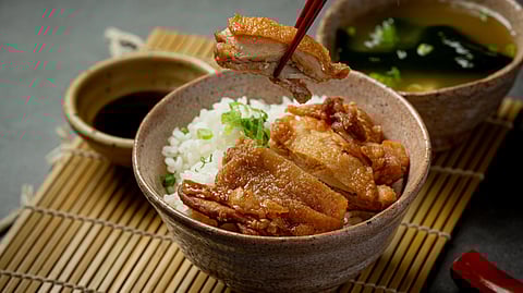 A bowl of rice with chopsticks next to a bowl of chicken.