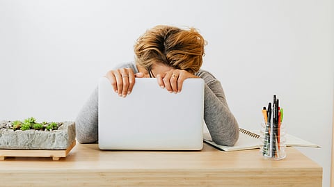 A woman sits at a desk, resting her head in her hands.