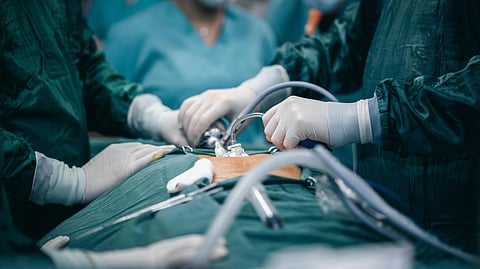 Surgeons in green scrubs and masks perform a procedure in an operating room.