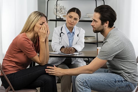 A woman is being consoled by a male in a doctor's office.