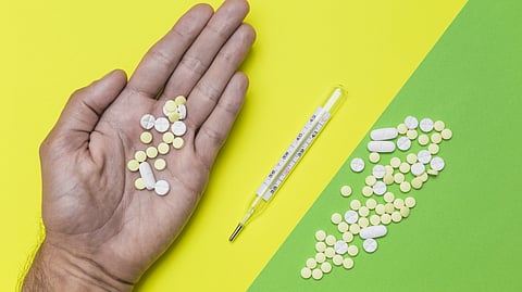 A person holding some pills in his palm on a yellow and green background.