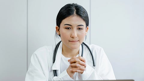 Portrait of a female doctor with a very tense expression, wearing a white coat and stethoscope, looking stressed and overwhelmed.