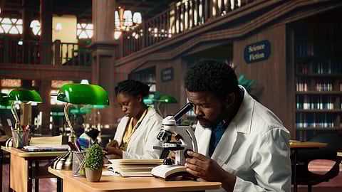 A man and a woman in lab coats work studiously at a library table. 