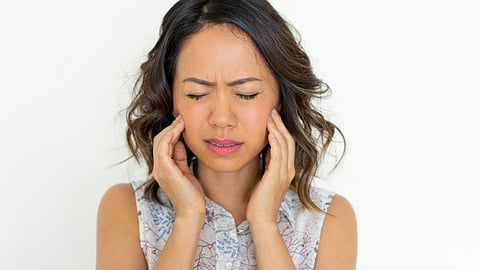A woman looking distressed because of jaw pain, touching her cheeks.