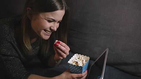A smiling woman enjoying popcorn while watching something on a tablet. 