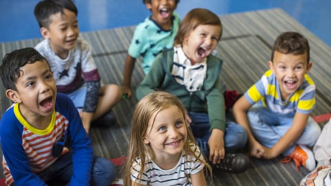 A bunch of happy small preschool children sitting on the floor in a classroom in UK.