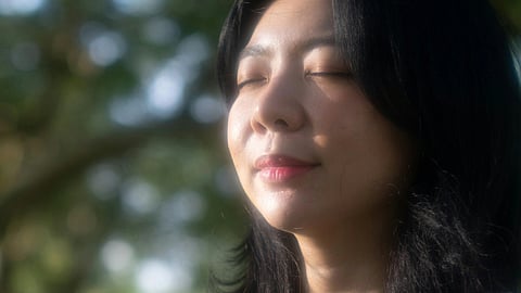A close up of a woman smiling in a garden having glimpses of sunlight on her face.