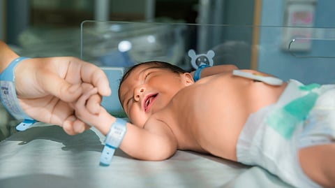 A newborn baby wearing a diaper lies on a hospital bed.