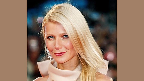 Portrait of actress Gwyneth Paltrow smiling and posing for a photograph while wearing a beige dress.
