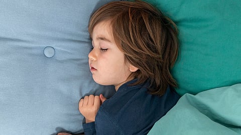 A young child sleeps peacefully under teal bedding.