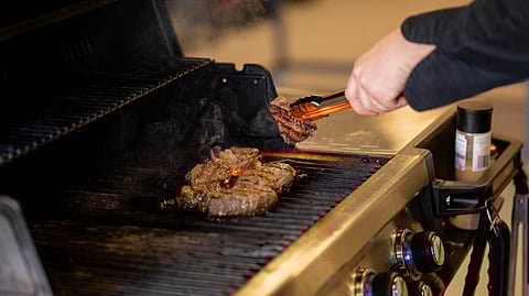 A person in black sleeves grills hamburgers on an outdoor barbecue.