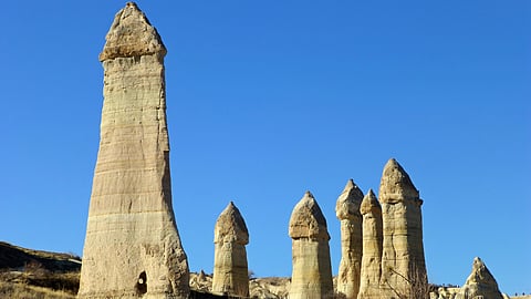Tall, uniquely shaped rock formations stand under a clear blue sky in Cappadocia, Turkey. 