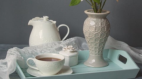 A soft pastel flower arrangement in a vase sits beside a teapot, cup, and sugar jar.