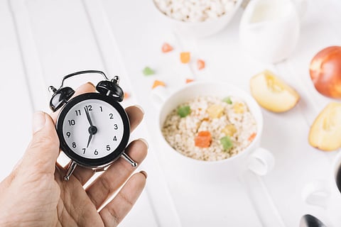 A small timepiece clock held in a hand and some food in the background. 