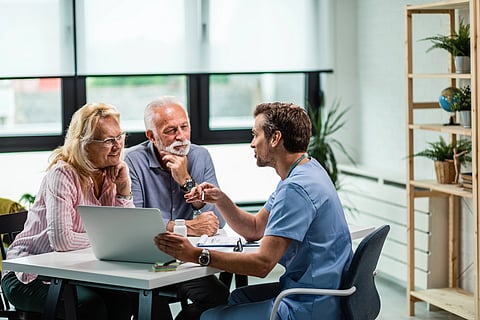 Happy old couple and their doctor communicating while using laptop during medical appointment.