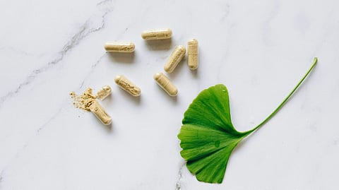 A brown powder-filled capsule broken open, spilling its contents on a marble surface, accompanied by a single green leaf.