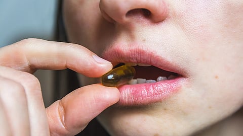 Close-up of a woman holding a brown capsule pill near partly open lips. 