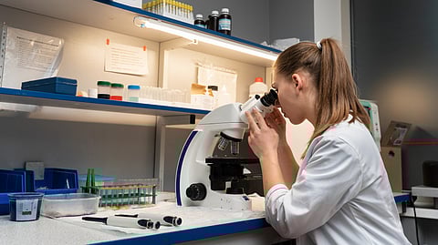 A scientist in a lab coat peers into a microscope in a laboratory setting.