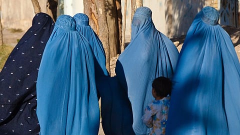 A group of women clad in blue burqa with a young girl in a frock walking along them.
