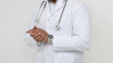 A man in a doctors coat with stethoscope around neck and wearing a watch in one hand.